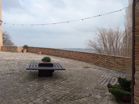 Un tranquillo cortile in pietra circondato da mura in mattoni, con piante ornamentali e un grande vaso centrale che aggiunge un tocco naturale all&rsquo;ambiente