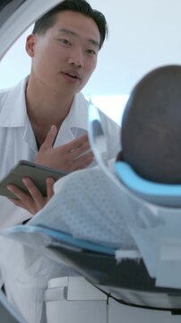 Vertical video: Raising hand, dentist in white coat explaining care at dental chair, holding tablet