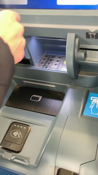 Customer hand tapping atm. Card slot and contactless reader, receipt and keypad visible, sleeve and fingertip gesture captured. 