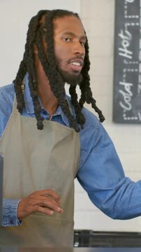Vertical video: Replying to customer, barista in apron in cafe tapping POS handing paper cup