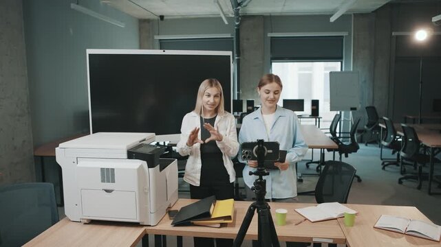 Business meeting with two women discussing projects in an office space with a printer and camera setup