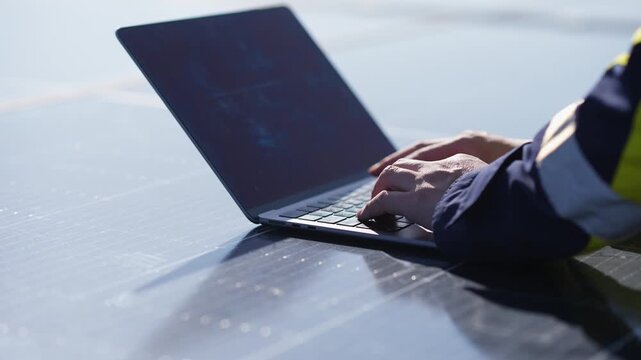 Worker using a laptop computer on a solar panel in outdoor field conditions