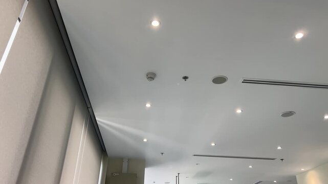 Modern office interior showcasing clean white ceiling with recessed background light, ventilation, and security camera