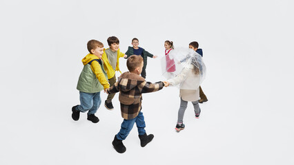 Children holding hands playing circle game around transparent umbrella wearing mid season kids...