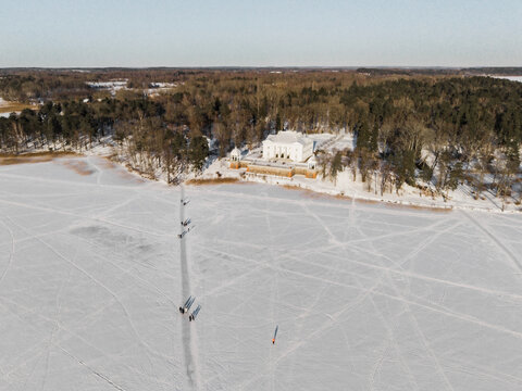Aerial view of a pristine white palace standing majestically on the snowy banks of the frozen Lake Galve, framed by the dark forest, Trakai, Lithuania.