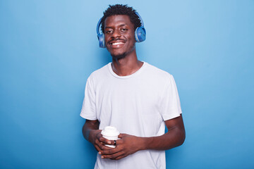 Portrait of african american individual wearing wireless headphones and holding a cup of coffee....