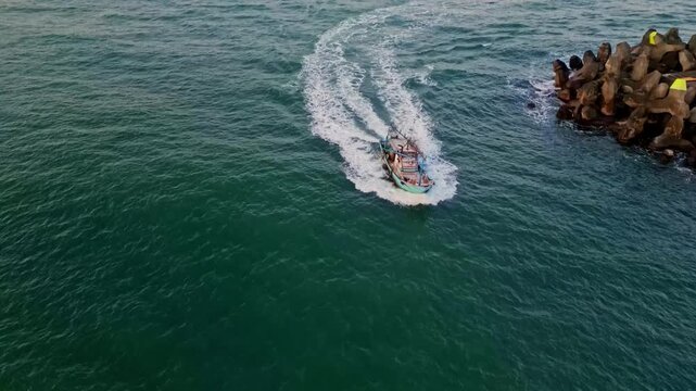 Aerial view of a boat cutting through the dark water, leaving a white wake as it approaches tetrapods on the coastline, Keelung, Keelung City, Taiwan.