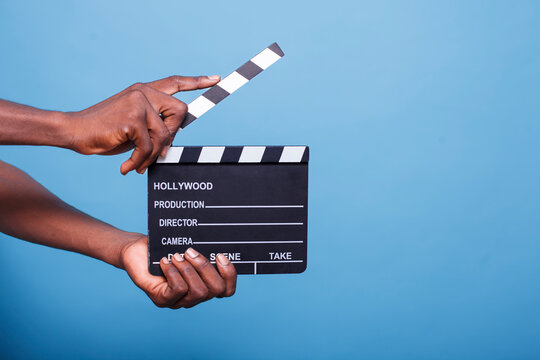 Close-up of african american hand clutching a clapperboard, used to cutting scenes for movies and the film business. Black person displays a movie chalkboard for film production.