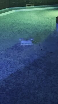 Robotic pool cleaner moving along bottom of swimming pool under blue green light cleaning tiles and removing dirt underwater. High quality 4k footage