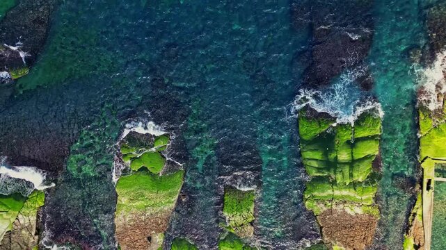 Aerial view of the vibrant green algae-covered Laomei Reef contrasting against the deep blue sea, creating a stunning natural scene, New Taipei City, Taiwan.