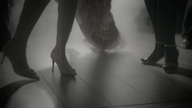 1920s old style black and white color group of people close-up legs body part dancing crowd in dark night club. girls flapper female male have fun at dance floor birthday party retro roaring twenties