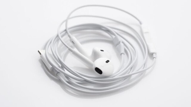 White wired in-ear headphones with USB Type-C connector rotating slowly on a seamless white background. 
