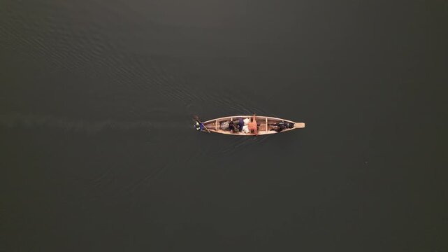 Aerial view of a wooden boat carrying people, cutting through the still, dark waters creating ripples, Suleja, Niger, Nigeria.