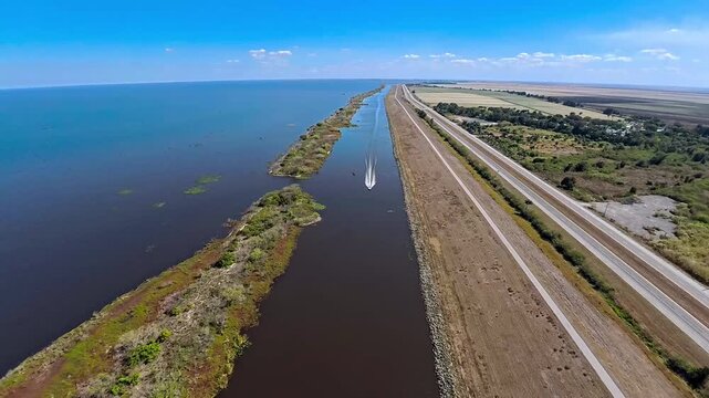 Aerial view of a boat speeding through the dark waters of Lake Okeechobee, leaving a white foamy trail, contrasted by vibrant green vegetation, Lake Harbor, Florida, United States.