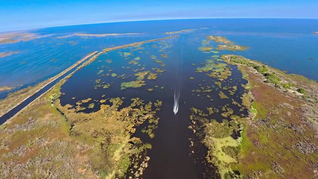 Aerial view of a boat speeding through a channel surrounded by marshland and the vast blue waters of Lake Okeechobee, Lake Harbor, Florida, United States.