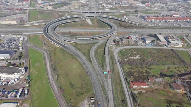 Aerial view of a complex highway interchange with cars and trucks, the grey concrete contrasting with patches of green vegetation, Kalochori, Thessaloniki, Greece.