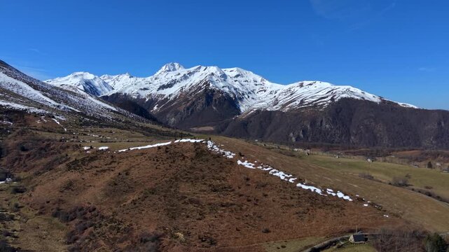 Aerial view of a landscape with mountains covered in snow under a clear blue sky, contrasting with the brown and green hills, Campan, Occitanie, France.
