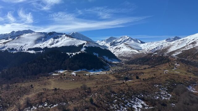 Aerial view of snow-capped mountains under a blue sky, the landscape reveals a mix of textures and tones, Campan, Occitanie, France.
