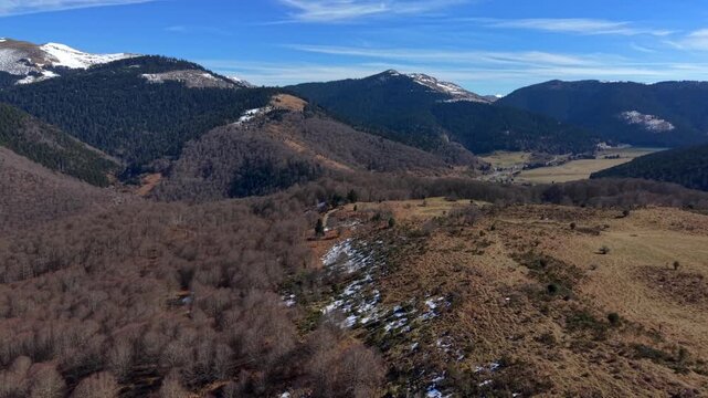 Aerial view of the undulating terrain with mountains, valleys, trees and meadows, a picturesque landscape filled with muted earthy tones, Campan, Occitanie, France.