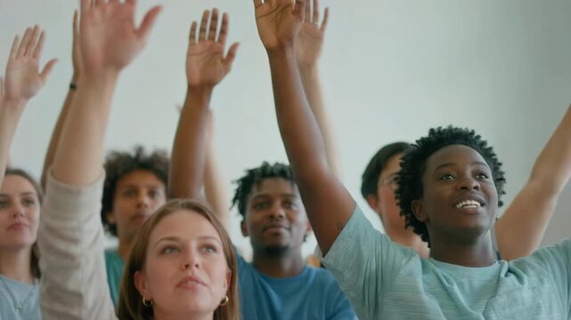 Diverse group of people raising hands together in an audience. Multicultural crowd volunteering or voting during a meeting. Students participating in a seminar or classroom