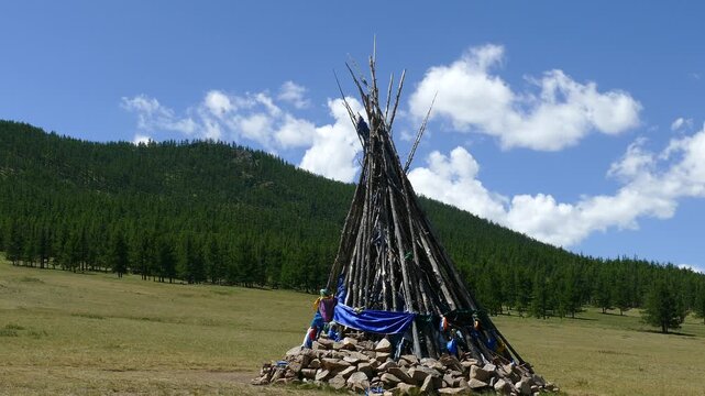 Ovoo (obo) is a sacred object in the form of a pile of stones and a hut of logs against the background of low, coniferous forests and picturesque cloudy skies. Typical Mongolian landscape.