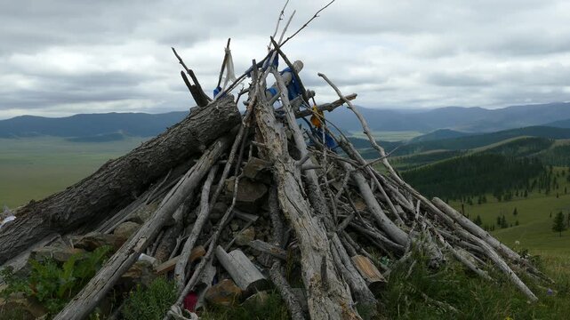 Obo (ovoo) is a sacred object in the form of a heap of stones and a hut of logs against the background of low, coniferous forests and picturesque cloudy skies. The Mongolian landscape.