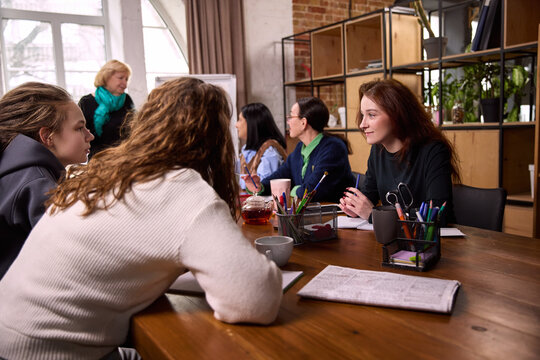 Young women discussing ideas at modern workspace table. Concept of creative collaboration, student teamwork, informal business meeting, startup development, coworking culture.