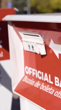 Young Man Deposits Mail-In Ballot Letter into Official Ballot Box Next to Drop Ballot Here Sign Vertical