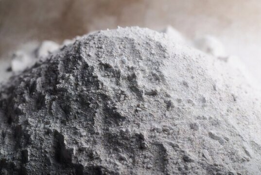 A pile of gray cement or concrete dust. It appears to be being poured or spread. A construction site or workshop.
