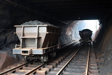 Fototapeta premium Two ore cars on a mine railway transport coal. It’s a dark, underground mining tunnel.