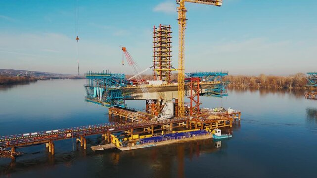 Aerial view of a bridge construction site over water, a symphony of steel and concrete against the serene blue river, Novi Sad, Vojvodina, Serbia.
