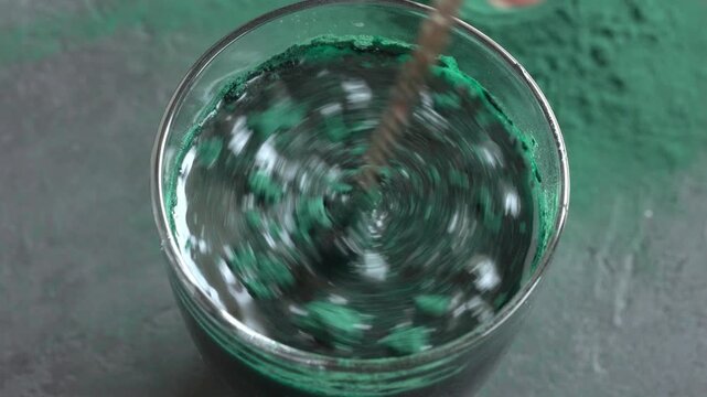 Stirring spirulina algae powder in a glass of water with a spoon. Nutritional supplement.