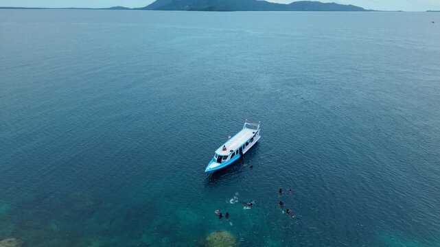 Aerial view of a boat sailing on the calm waters near Cemara Kecil Snorkeling Spot with people snorkeling, contrasting with the distant islands, Karimunjawa, Central Java, Indonesia.