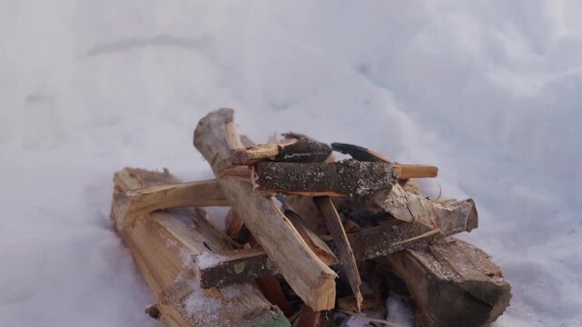 Small campfire burning inside a snow pit surrounded by deep winter snow. Firewood slowly burns while light smoke rises into the cold air. High quality 4k footage