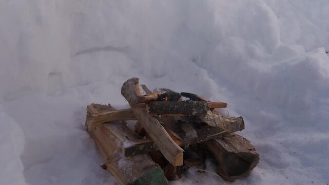 Small campfire burning inside a deep snow pit during winter. Firewood slowly burns while thin smoke rises into the cold air surrounded by high snow walls. High quality 4k footage