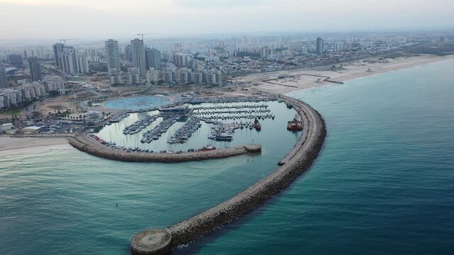 Aerial view of the Ashdod Marina with boats and a long rock pier extending into the sea contrasting with the city skyline, Ashdod, South District, Israel.