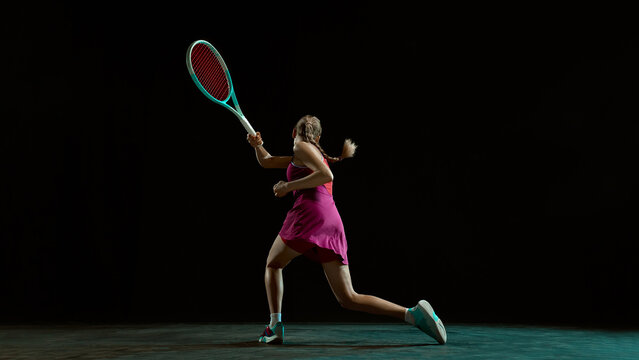 Athletic woman tennis player preparing backhand shot in dramatic studio lighting. Concept of precision, control, discipline, modern sports advertising, professional training, and competitive mindset.