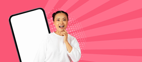 A woman stands happily with her hand on her chin near a large smartphone. She wears a white shirt and shows her excitement. The background is colorful with a bright pink theme. © Prostock-studio