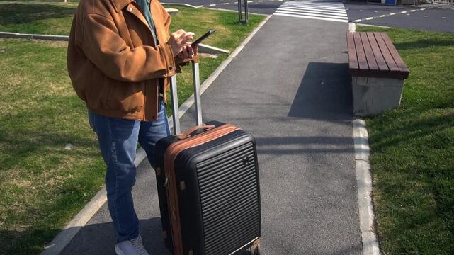 Woman holds a mobile phone in her hands and checks the check-in time through the app. Woman with a suitcase calls a taxi to the airport