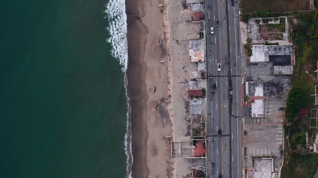 Aerial view of a serene beach meeting a road, remnants of buildings and cars are visible, creating a contrast between nature and infrastructure, Malibu, California, United States.