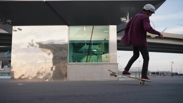 Young stylish skateboarder in helmet performs a kickflip on a city street amid modern architecture, capturing energetic urban lifestyle, skillful motion and youthful freedom