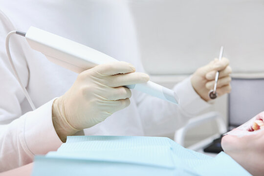 Dentist holds portable 3D scanner in his hand to examine the jaw and oral cavity. The dentist performs an intraoral scan before installing ceramic veneers and crowns. The concept of digital dentistry.