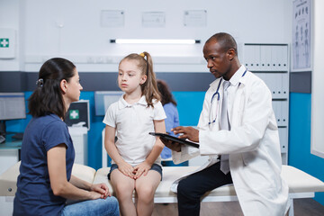 Fototapeta premium African American doctor provides healthcare advice. Digital tablet assisting with communication and recording of patients information by male physician. Comforting healthcare environment.