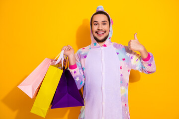 Happy man in pastel star pajama jumpsuit shopping bags on bright yellow background