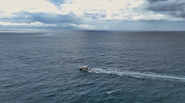 Aerial view of a boat sailing on the vast, deep blue ocean leaving a white foamy trail under a cloudy sky, Tambor, Puntarenas Province, Costa Rica.