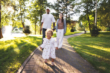 Happy family with small child walking together in green park at sunset. Warm summer outdoors with...