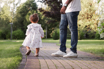 Fototapeta premium Dad with kid. Small child walking away from father during park stroll, back view. Candid family moment outdoors, parenting, independence. Natural lifestyle childhood exploration in summer nature