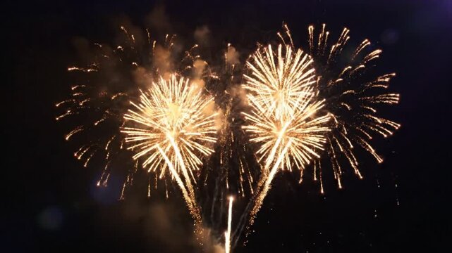 Bright golden fireworks exploding in the dark night sky during celebration with loud sound and stunning effects
