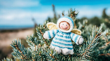 Naklejka premium Knitted angel doll with wings perched on a green conifer branch, symbolizing Christmas spirit and holiday joy outdoors