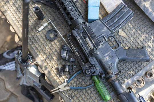 Close up of black assault rifle disassembled on workbench for maintenance. firearm part, gunsmithing tool, and weapon repair create focused and serious mood